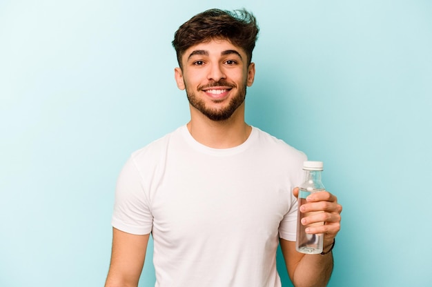 Giovane uomo ispanico in possesso di una bottiglia d'acqua isolata su sfondo bianco felice sorridente e allegro