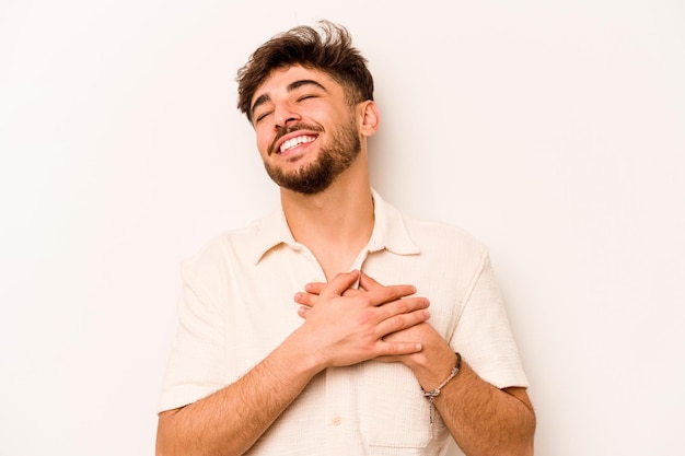 Giovane uomo ispanico isolato su sfondo bianco che ride tenendo le mani sul concetto di felicità del cuore