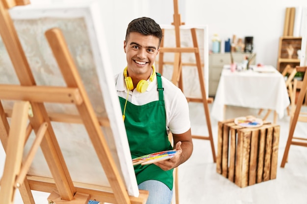 Giovane uomo ispanico sorridente disegno fiducioso in studio d'arte