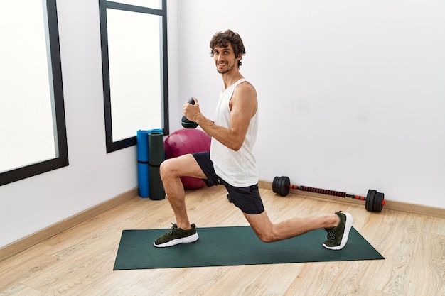 Giovane uomo ispanico sorridente formazione fiduciosa utilizzando kettlebell presso il centro sportivo