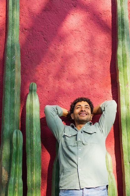 Giovane uomo ispanico sorridente in piedi contro un muro con cactus