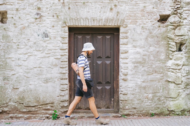 Giovane uomo latino con un cappello a secchiello che passa davanti a una vecchia porta della città coloniale