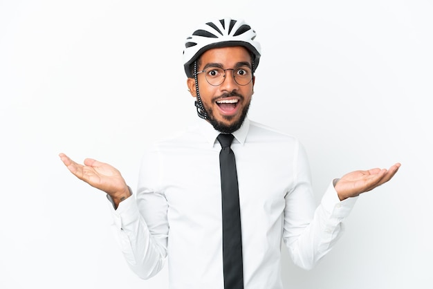 Giovane uomo latino d'affari in possesso di un casco da bici isolato su sfondo bianco con espressione facciale scioccata