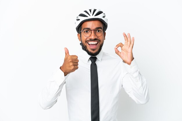 Giovane uomo latino di affari che tiene un casco da bici isolato su sfondo bianco che mostra il segno giusto e il gesto del pollice in su