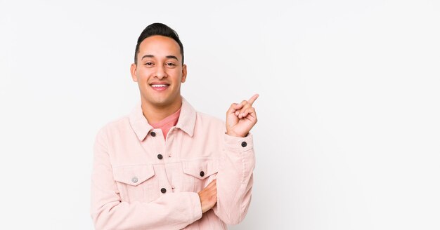 Giovane uomo latino in posa isolato sorridendo allegramente indicando con l'indice di distanza.