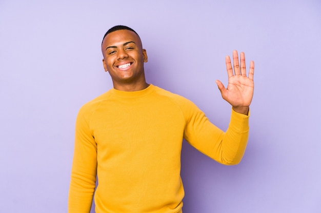 Giovane uomo latino isolato sul muro viola sorridente allegro che mostra il numero cinque con le dita.