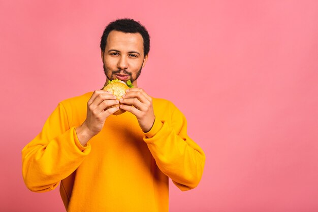 Giovane uomo mangiare hamburger isolato su rosa