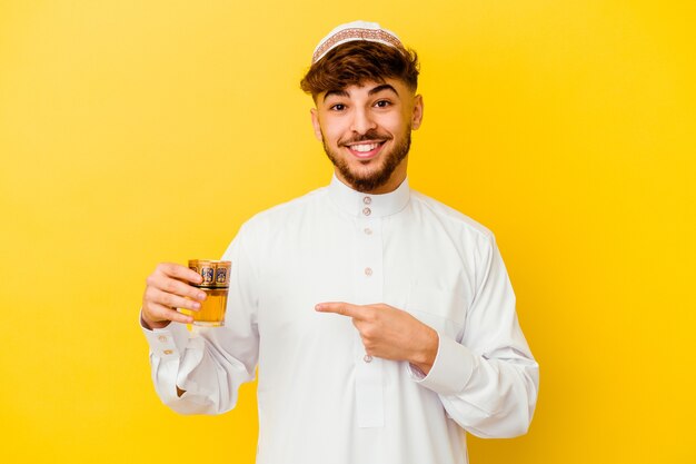 Giovane uomo marocchino che indossa il tipico costume arabo bere il tè isolato su sfondo giallo