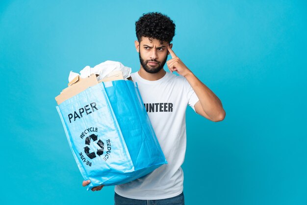 Giovane uomo marocchino che tiene un sacchetto di riciclaggio pieno di carta da riciclare isolato