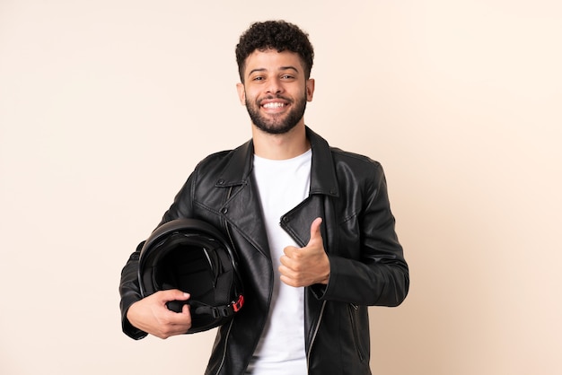 Giovane uomo marocchino con un casco da motociclista isolato sulla parete beige che dà un pollice in alto gesto