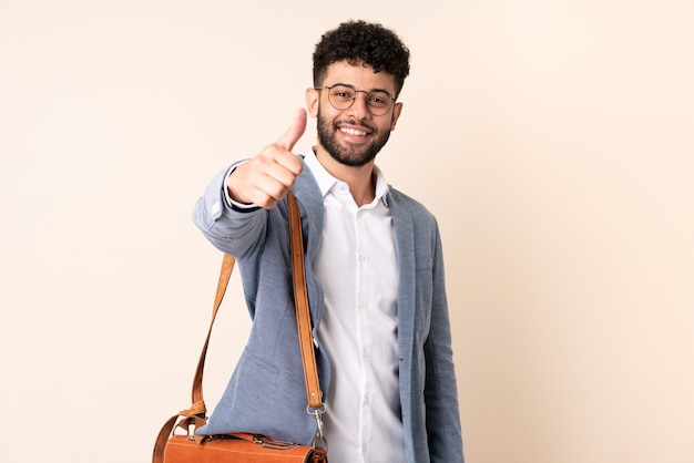 Giovane uomo marocchino di affari isolato sul muro beige con i pollici in su perché è successo qualcosa di buono