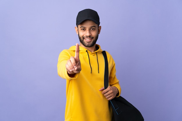 Giovane uomo marocchino di sport con borsa sportiva isolata sulla parete viola che mostra e che alza un dito