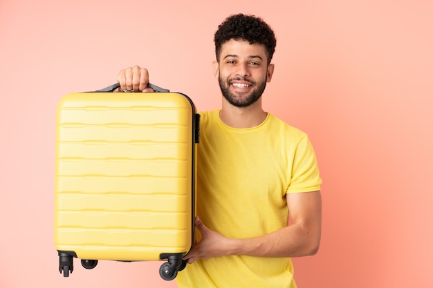 Giovane uomo marocchino isolato su sfondo rosa in vacanza con la valigia da viaggio