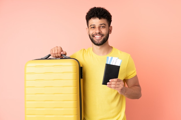 Giovane uomo marocchino isolato sulla parete rosa in vacanza con la valigia e il passaporto