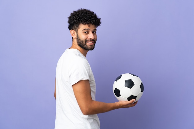 Giovane uomo marocchino isolato sulla parete viola con pallone da calcio