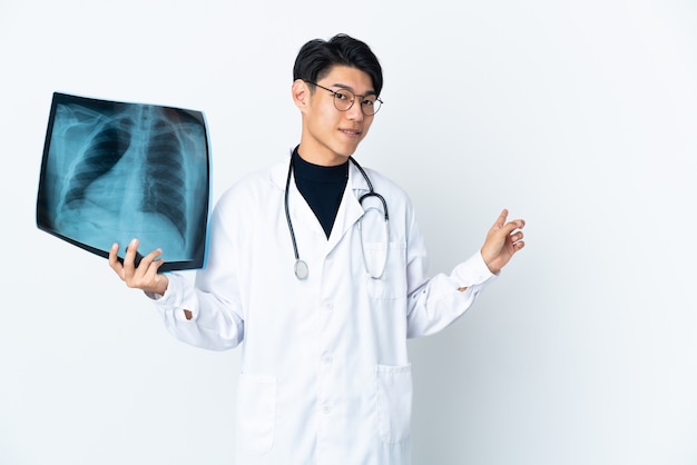 Giovane uomo medico cinese che tiene la radiografia isolata sulla parete bianca che indica indietro