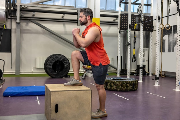 Giovane uomo muscoloso che si allena con una scatola di legno si allena in palestra crossfit