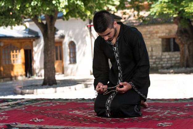 Giovane uomo musulmano che fa la tradizionale preghiera a Dio mentre indossa un cappello tradizionale Dishdasha