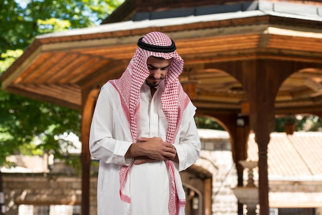 Giovane uomo musulmano che fa la tradizionale preghiera a Dio mentre indossa un cappello tradizionale Dishdasha