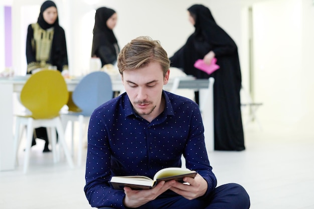 giovane uomo musulmano seduto sul pavimento mentre legge il libro sacro Corano prima della cena iftar durante una festa del ramadan a casa