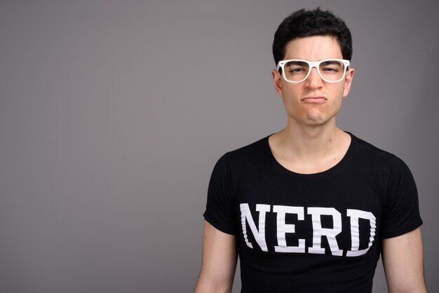 Giovane uomo nerd bello con gli occhiali contro il grigio