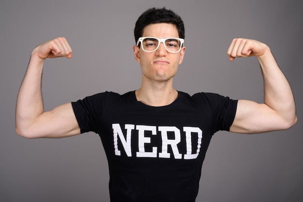 Giovane uomo nerd bello con gli occhiali contro il grigio