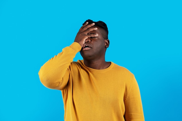 Giovane uomo nero che fa il gesto Facepalm mentre sta in piedi isolato su sfondo blu