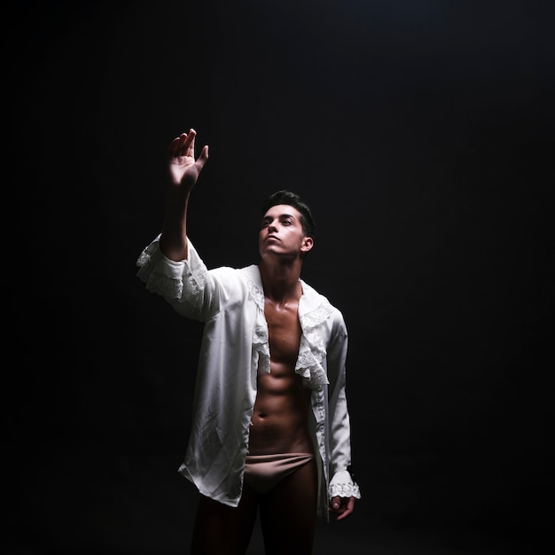 Giovane uomo nudo in camicia bianca aperta che solleva la mano