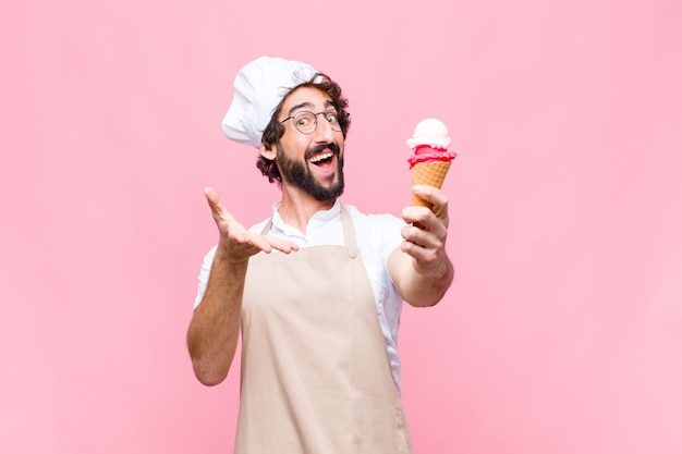 Giovane uomo pazzo del cuoco unico con un gelato contro la parete rosa