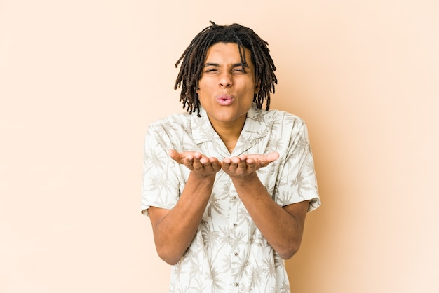 Giovane uomo rasta afroamericano piegando le labbra e tenendo le palme per inviare un bacio d'aria.