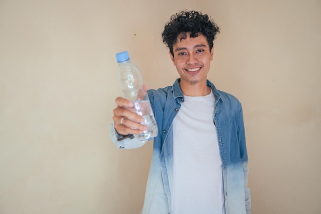 Giovane uomo riccio con abiti in denim tiene una bottiglia d'acqua Sorriso applausi ed espressione felice