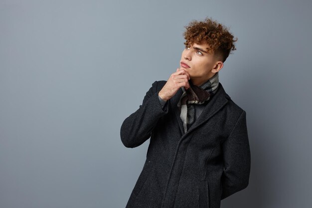 Giovane uomo riccio in un cappotto in studio in posa su uno sfondo grigio