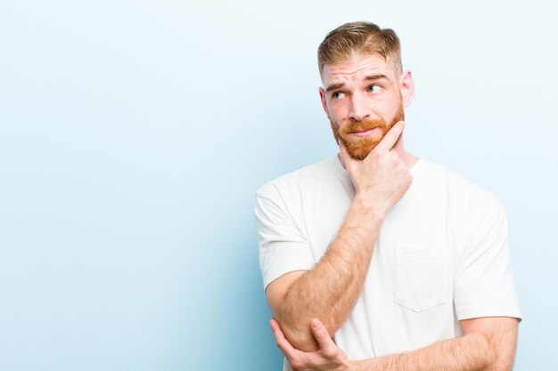 Giovane uomo rosso che sorride felicemente e che sogna ad occhi aperti o dubita, guardando al lato