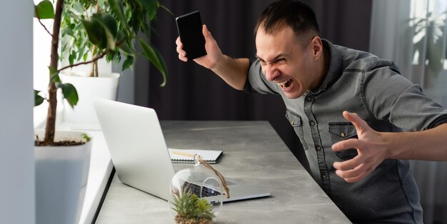 Giovane uomo scioccato vestito con una camicia mentre utilizza il laptop. su grigio.