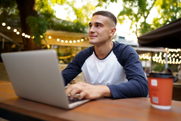 Giovane uomo seduto al tavolo e digitando sulla tastiera del laptop mentre si lavora in un caffè all'aperto