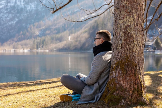 Giovane uomo seduto all'aperto e godersi le montagne neve lago bel tempo cielo blu sole bellissimo paesaggio Tempo con te stesso sognando relax salute mentale Turismo vacanze e viaggi