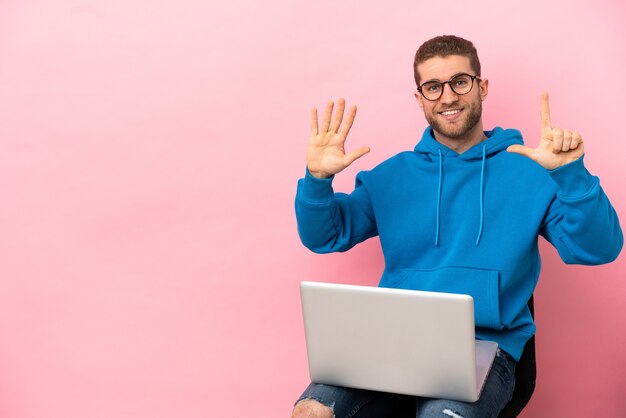 Giovane uomo seduto su una sedia con il computer portatile che conta sette con le dita