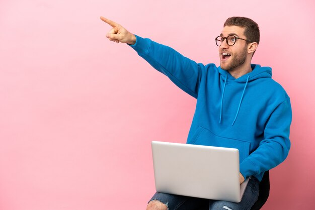 Giovane uomo seduto su una sedia con il laptop rivolto lontano