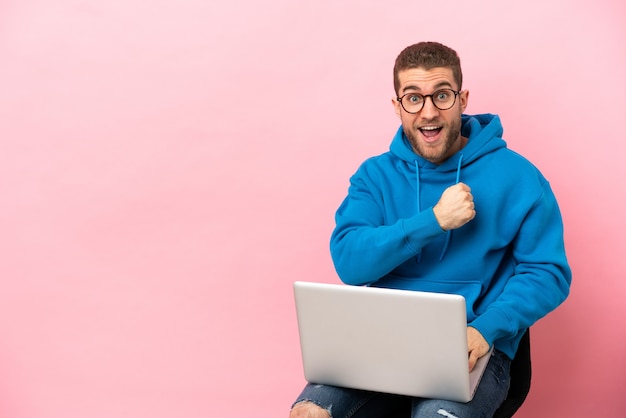 Giovane uomo seduto su una sedia con un computer portatile che celebra una vittoria