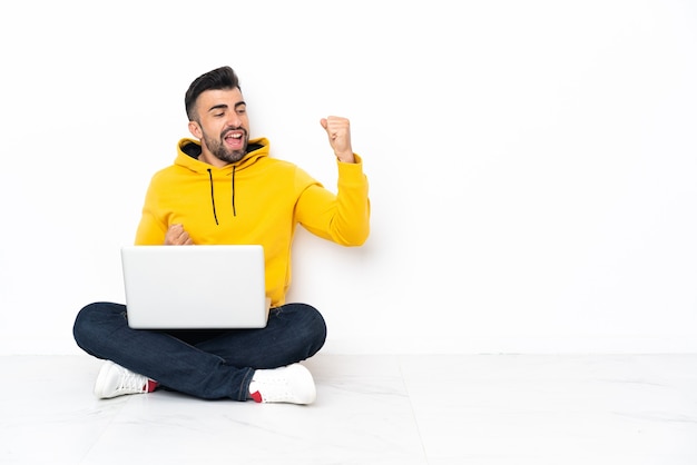 Giovane uomo seduto sul pavimento con il suo laptop che celebra una vittoria