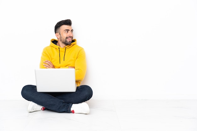 Giovane uomo seduto sul pavimento con il suo laptop guardando il lato