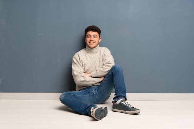 Giovane uomo seduto sul pavimento tenendo le braccia incrociate in posizione frontale