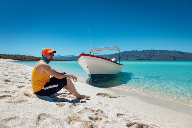 Giovane uomo seduto sulla spiaggia paradisiaca con sabbia bianca mare turchese e cielo blu Playa Isla Coronado Messico