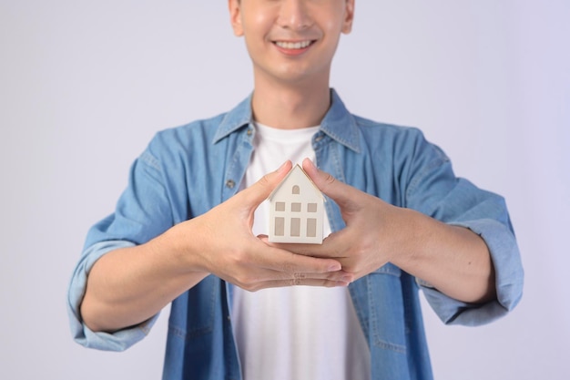 Giovane uomo sorridente azienda piccolo modello di casa su sfondo bianco studiox9