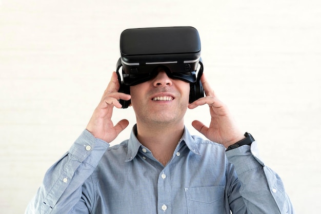 Giovane uomo sorridente che indossa maglietta e cuffie per realtà virtuale o occhiali VR che giocano a videogiochi su sfondo bianco