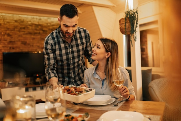 Giovane uomo sorridente che serve la cena alla sua ragazza nella sala da pranzo