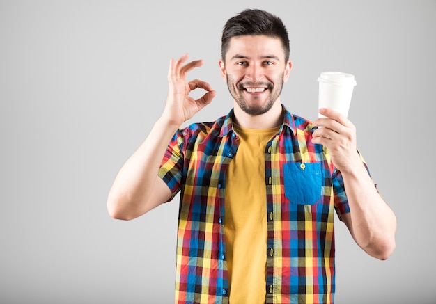 Giovane uomo sorridente con la tazza di caffè che mostra segno GIUSTO