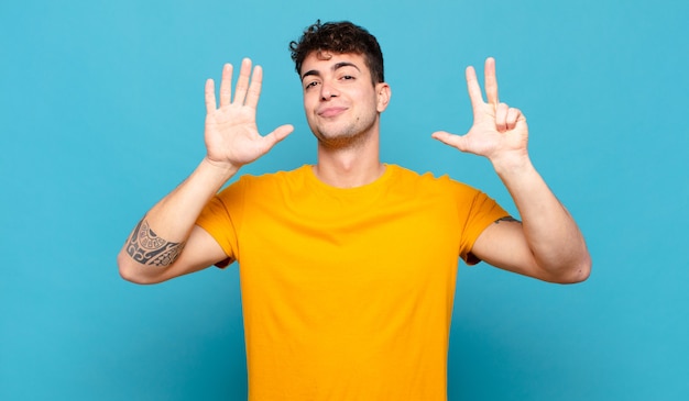 Giovane uomo sorridente e guardando amichevole, mostrando il numero otto o ottavo con la mano in avanti, conto alla rovescia