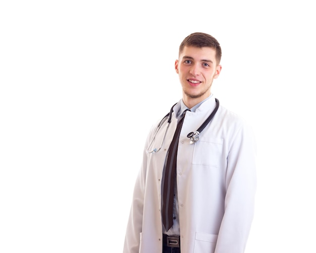 Giovane uomo sorridente in abito medico con uno stetoscopio sul collo su sfondo bianco in studio