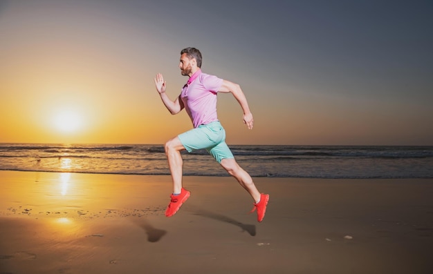 Giovane uomo sportivo americano atletico e in forma che fa allenamento in esecuzione sul tramonto al jogg di allenamento in spiaggia